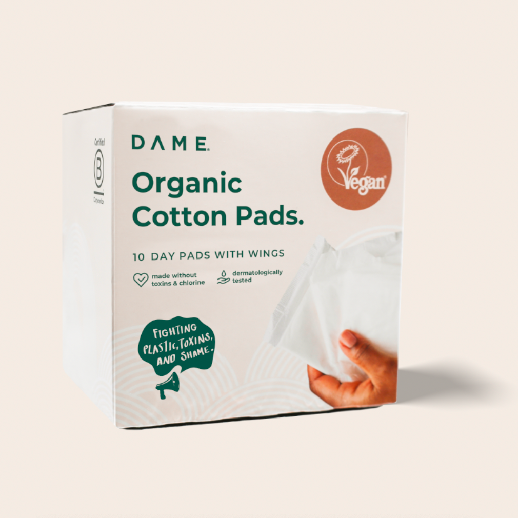 Packaging for Dame Organic Cotton Pads, showing a box with the product name and a hand holding a white pad with wings.