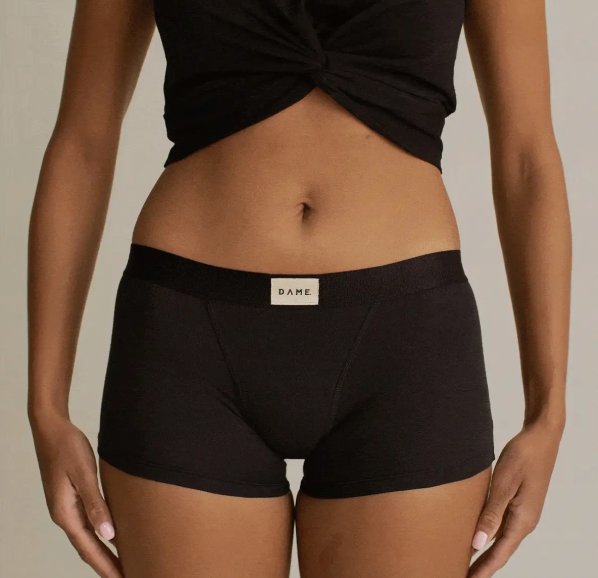 Person wearing black DAME period underwear with a visible brand label on a neutral background